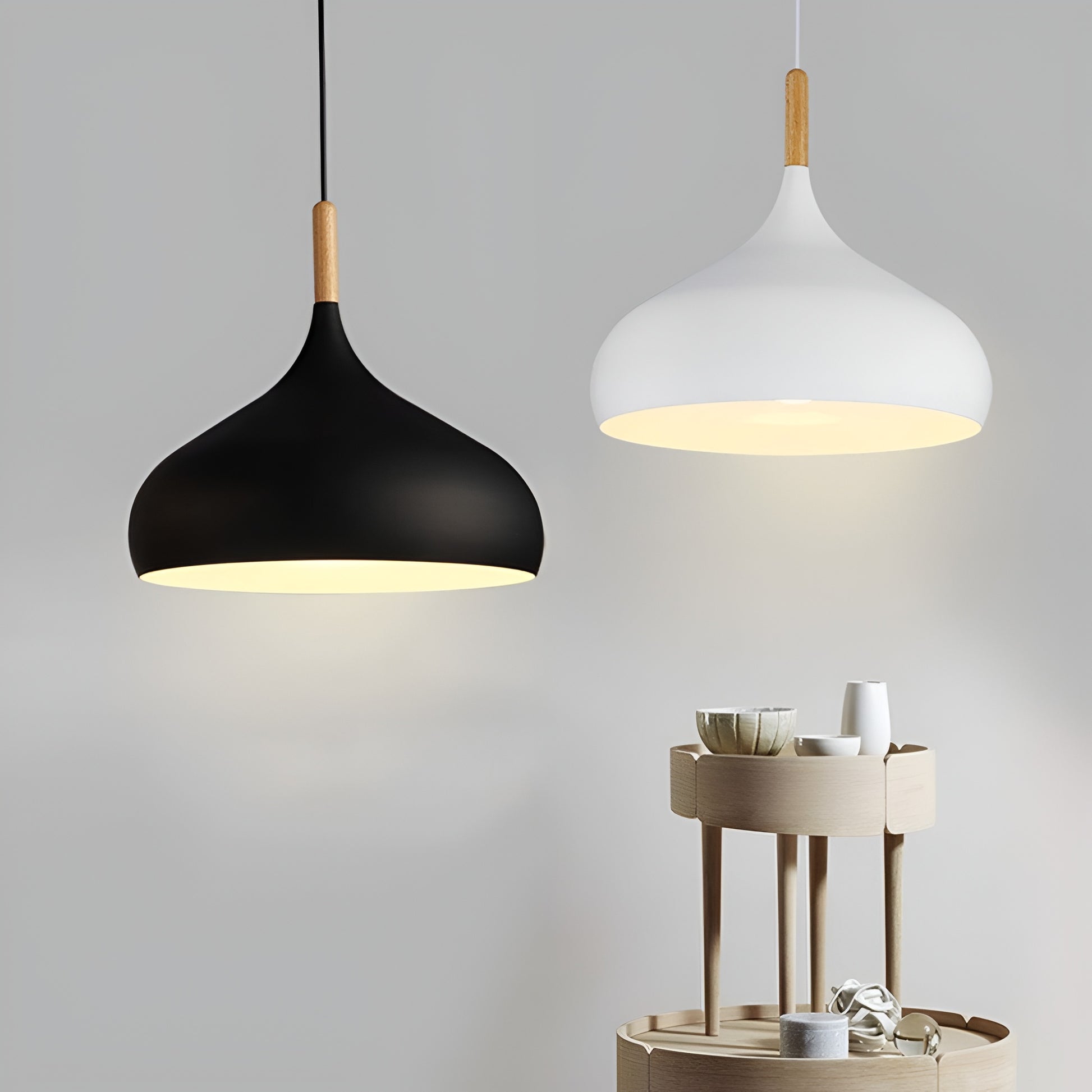 Two pendant lights, one black and one white, hanging against a gray background with a small table and items below.